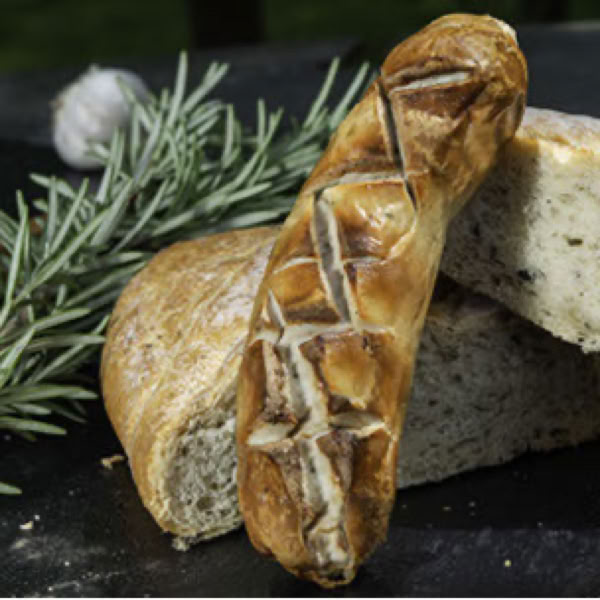 Brotlaib und geschnittenes Brot auf einem Tisch mit Rosmarinzweigen und einer Knoblauchknolle im Hintergrund.
