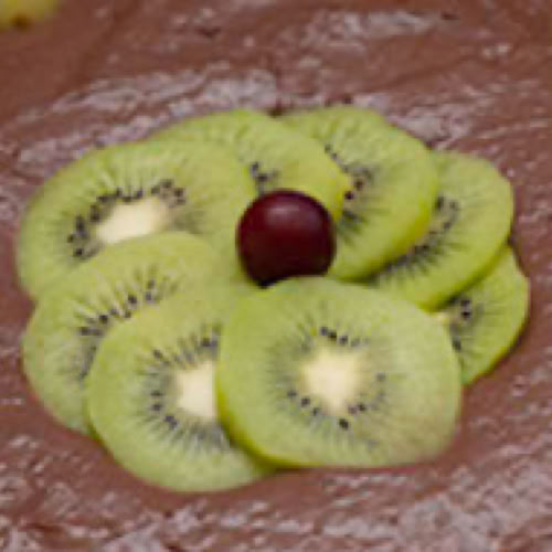 Schokoladenkuchen mit Kiwi-Scheiben und einer Kirsche in der Mitte.